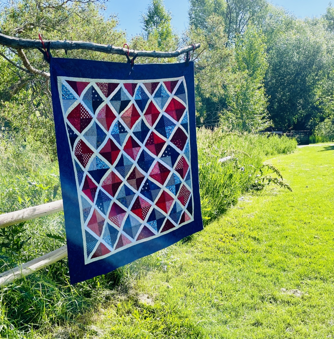 patriotic quilt hanging in tree in front of fence